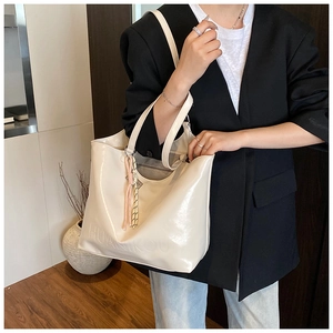 Detail view of cream patent leather tote bag with brand embossing and woven charm