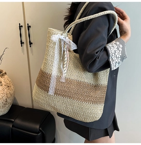 Detail of striped woven straw tote bag featuring a beige lace bow charm accessory
