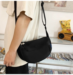 Detail of minimalist black half-moon crossbody bag showing nylon texture and wide strap