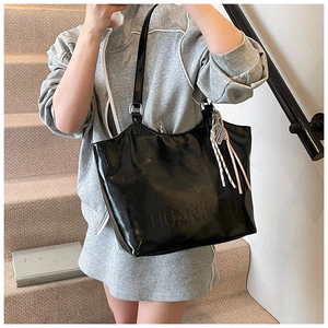 Close-up of black patent leather tote bag with embossed logo and woven tassel detail