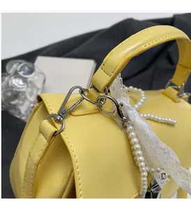 Close-up of bright yellow leather handbag with silver hardware and pearl lace charms
