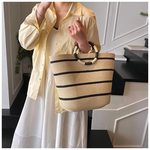 Detail of summer woven straw tote bag with black stripes and circular handle on model