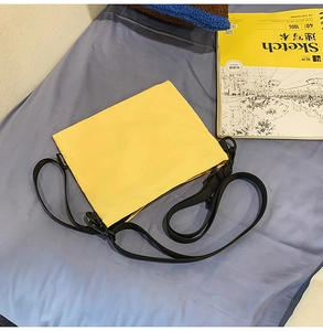 Detail of yellow minimalist envelope crossbody bag with adjustable black nylon strap