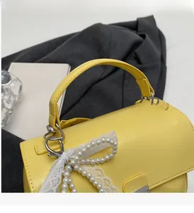 Detail of yellow handbag with pearl bow and silver hardware on a gray background