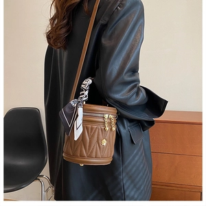 Close-up of brown quilted bucket bag with silk scarf handle and golden flower charm
