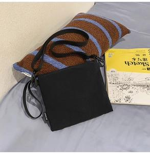 Detail of minimalist black canvas square crossbody bag with brand label and nylon strap