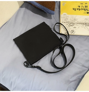 Detail of minimalist black nylon envelope bag with adjustable strap on grey fabric background