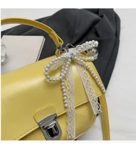 Close-up of yellow leather square bag featuring silver twist lock and pearl lace bow charm