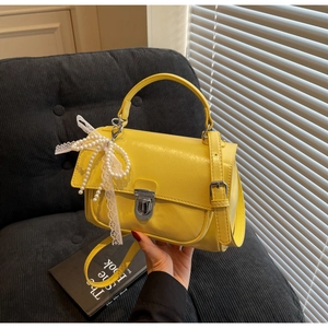 Detail of yellow square handbag with pearl lace bow charm and silver metallic buckle