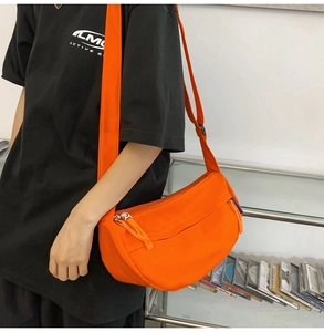 Detail view of bright orange crossbody bag with wide strap and silver metal zipper