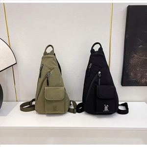 Detail view of olive green and black canvas chest bags with bunny head embroidery