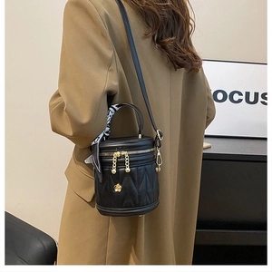 Detail of black quilted bucket bag with gold hardware and silk scarf on handle