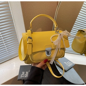 Detail of yellow crossbody bag with pearl lace bow charm and silver snap closure