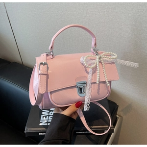 Detail of pink glossy leather handbag featuring silver lock and pearl bow charm