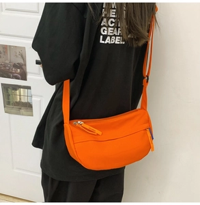 Detail view of a vibrant orange crescent crossbody bag made of durable nylon with wide strap