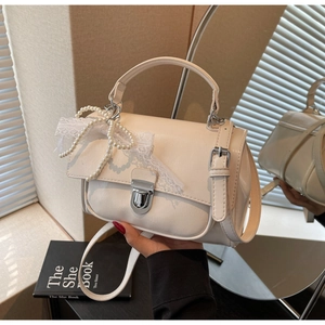 Detail of elegant cream shoulder bag with pearl bow and lace decoration on front flap