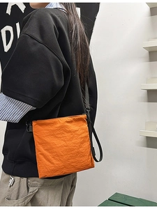 Bright orange envelope crossbody bag in nylon material with adjustable shoulder strap