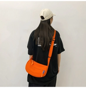 Detail of a bright orange crossbody half-moon bag featuring durable nylon and adjustable strap