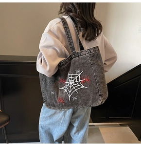 Detailansicht der grauen Denim-Tasche mit weißer Spinnennetz- und roter Spinnenstickerei