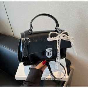 Detail of black glossy handbag with pearl lace bow and silver metal clasp lock