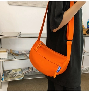 Side view of a bright orange nylon half-moon crossbody bag with an adjustable wide strap