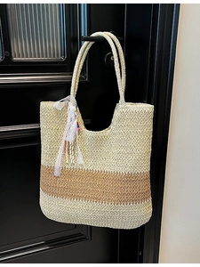 Large straw woven tote bag in contrast colors with lace ribbon, hanging on door handle