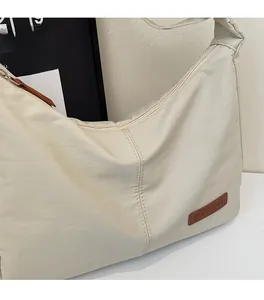 Macro shot of beige nylon shoulder bag showing soft pleated fabric and leather logo detail