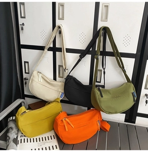 Detail of five crescent nylon crossbody bags in various colors on a metal bench