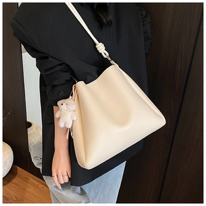 Détail du sac seau blanc cassé avec texture litchi, bandoulière nouée et breloque ours