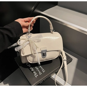 Close-up of minimalist cream square bag with pearl lace bow charm and silver lock