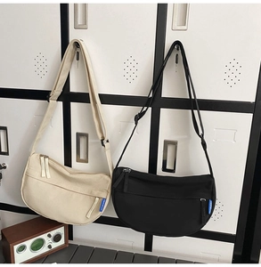 Detail view of canvas crescent crossbody bags in black and beige with adjustable wide straps