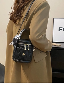 Quilted black bucket bag with golden camellia logo and silk scarf on a chic model