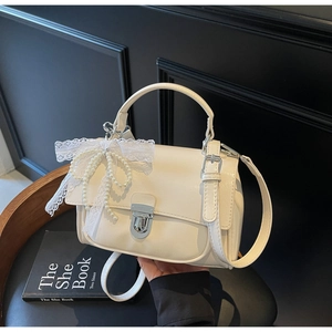 Detail of cream crossbody bag with lace bow, pearl charm, and silver twist lock