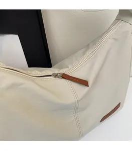 Close-up of smooth silver zipper with brown leather puller on cream shoulder bag