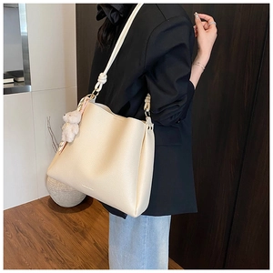 Détail du sac seau blanc cassé avec texture litchi, poignée nouée et breloque ours peluche