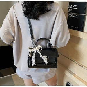 Detail of glossy black handbag with silver clasp, lace bow, and pearl charm accents