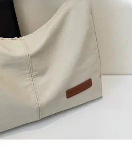 Close-up of cream white canvas tote bag material and brown leather logo patch details