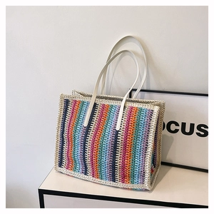 Detailed close-up of colorful striped handmade woven straw tote with white faux leather straps