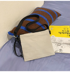 Détail du sac bandoulière beige clair avec sangle noire réglable et étiquette de marque