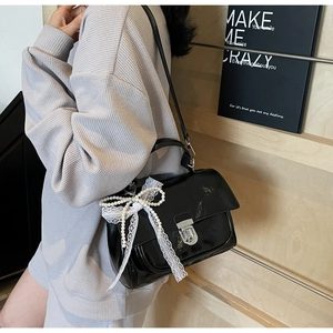 Detail of black glossy handbag with pearl string and white lace bow decoration