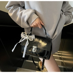 Detailed shot of black patent leather square bag with pearl lace bow decoration
