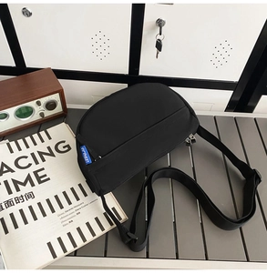 Detail view of the black nylon crossbody bag with adjustable strap and blue logo label