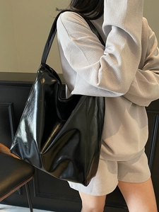 Minimalist black glossy leather tote bag shown on a model in a modern urban setting