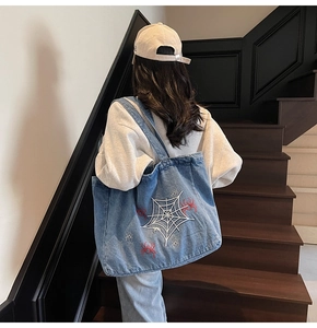 Detail view of spider web embroidery on blue denim tote bag with street fashion style