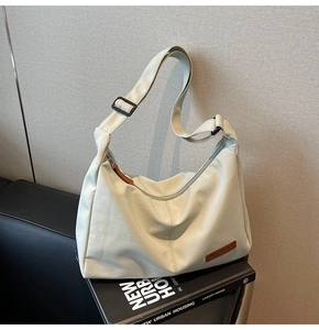 Detail of cream canvas tote bag showing black adjustable strap and brand leather patch