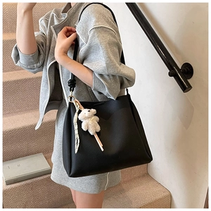 Détail du sac seau noir en cuir grainé avec bandoulière nouée et breloque peluche ours