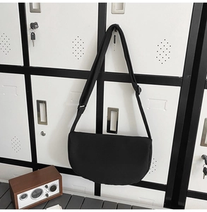 Detail of black crescent crossbody bag with adjustable wide strap on white cabinet