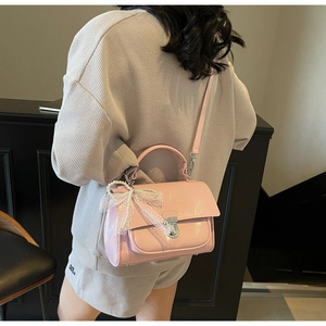 Detail of pink patent leather handbag with silver clasp and pearl bow charm on model