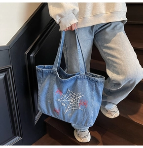 Detail of blue denim tote bag with spider web embroidery and red spider motifs on front