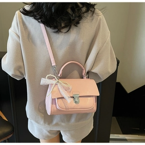 Pink patent leather crossbody bag with lace bow and pearl chain on a model